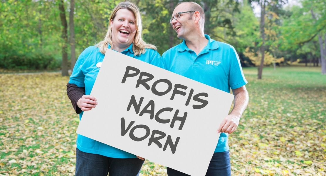 IPT - Intensivpflegeteam: Profis nach vorn Zwei Mitarbeiter der IPT halten ein Schild hoch und bieten Pflegejobs in Würzburg, Schweinfurt, Karlstadt.