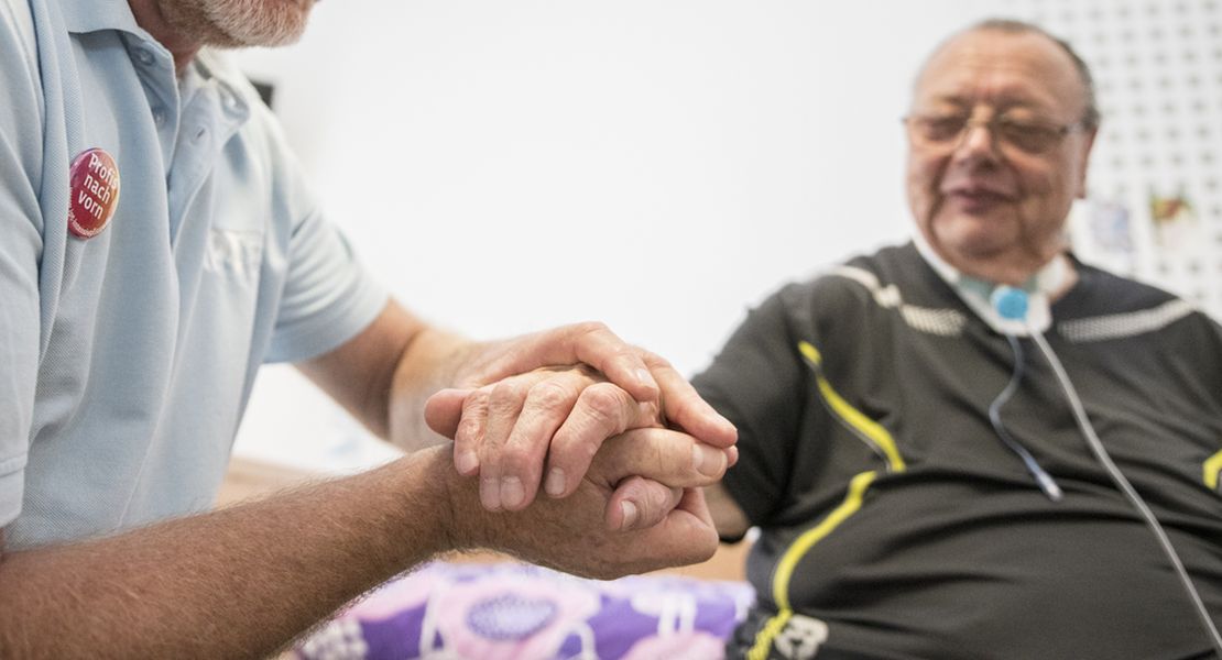 Leben mit Intensivpflege Pflegekraft hält die Hand eines WG-Bewohners. So lebt es sich mit Intensivpflege.